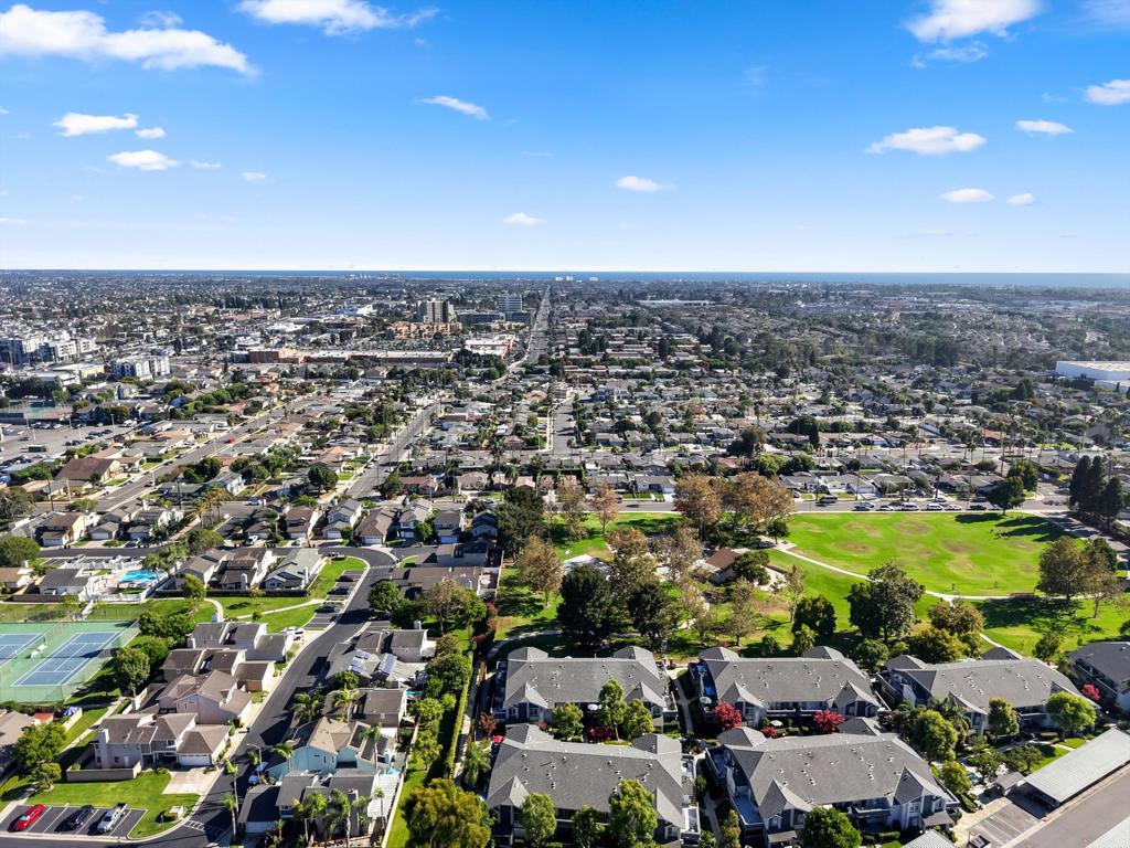 Aerial view of homes beside a green park and tennis courts, with the city stretching to the horizon.