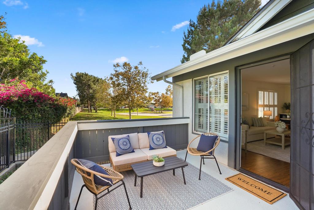 Furnished condo balcony overlooking a landscaped lawn, with woven chairs and a pale sofa.