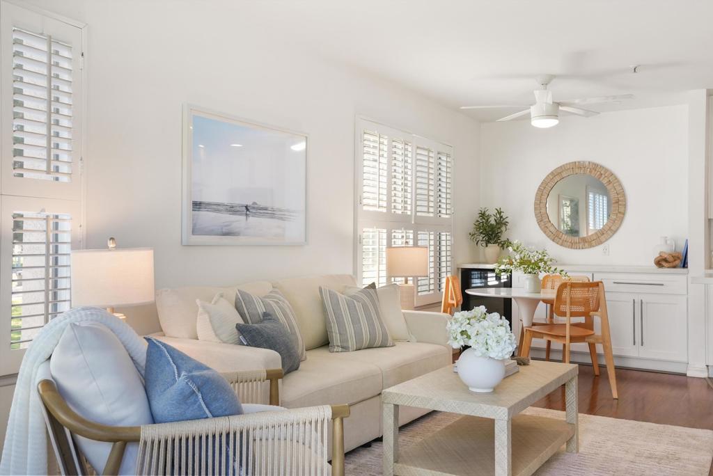Staged living and dining area with plantation shutters, a beige sofa, and a round wall mirror.