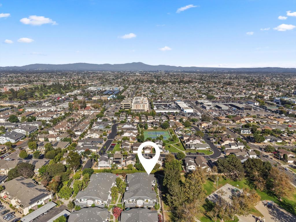 Aerial neighborhood view with a map pin marking a home, commercial buildings, and distant hills.