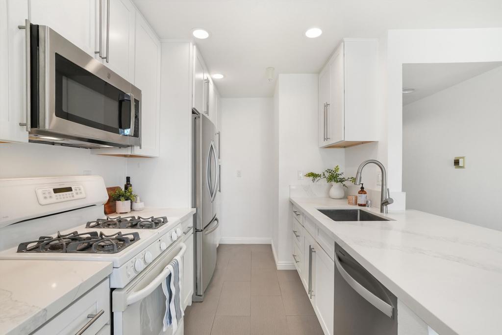 Bright white kitchen with stainless steel appliances and a long quartz peninsula with sink.