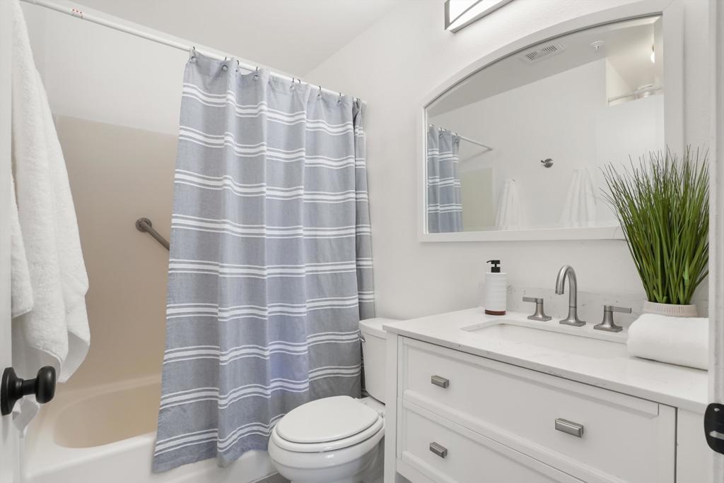 Bathroom with a gray striped shower curtain, bathtub, toilet, and white vanity.