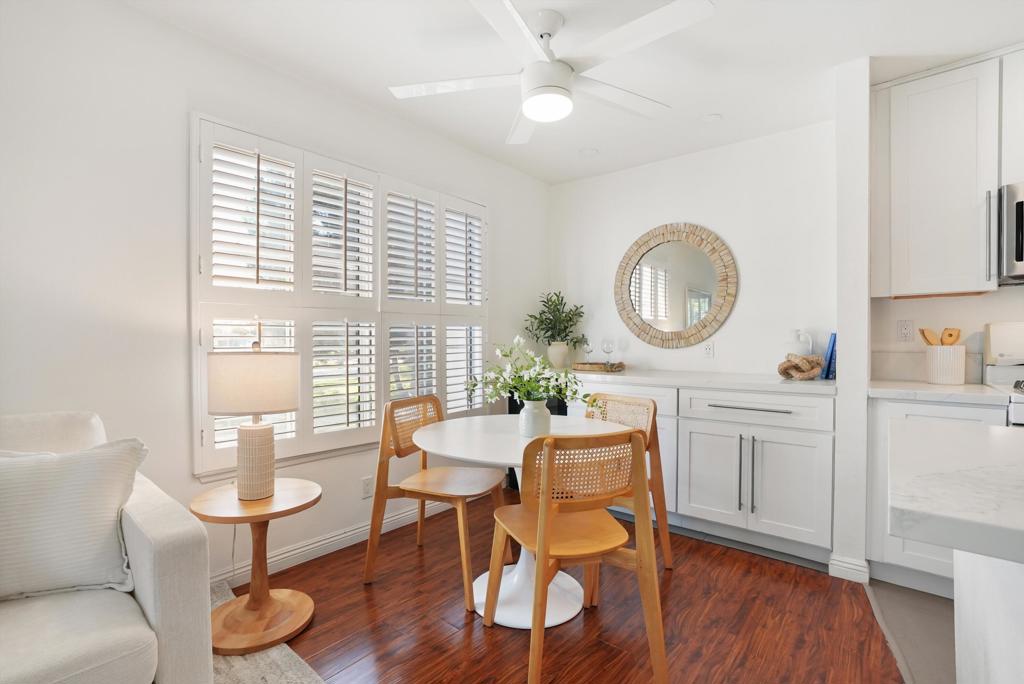Dining area with a round table, wooden chairs, plantation shutters, and reddish wood flooring.