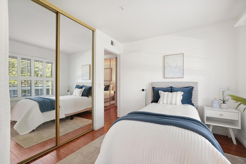 Bedroom with mirrored closet doors, a white bed, blue accents, and hardwood floors.