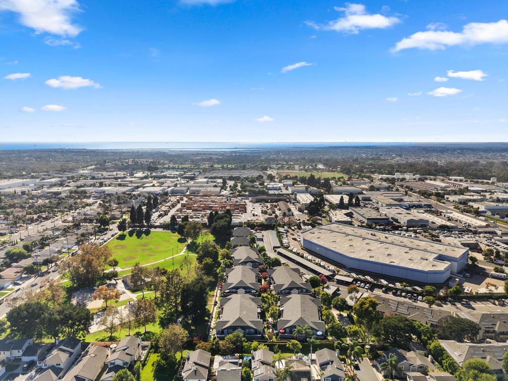 Aerial view of Huntington Beach homes, a nearby park, commercial buildings, and the ocean on the horizon.