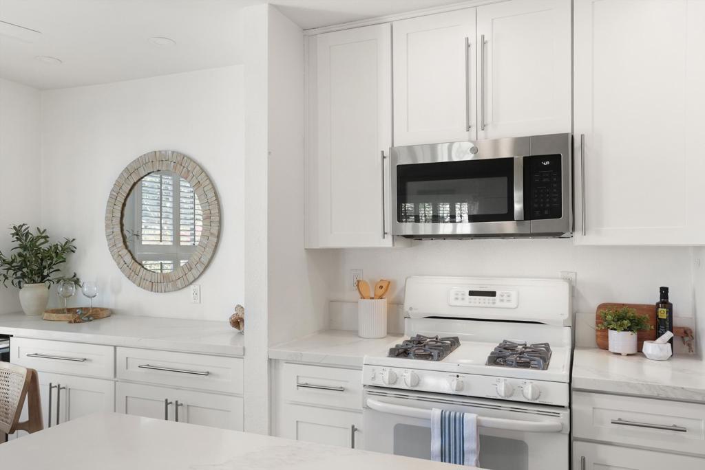 White kitchen with a gas range, stainless steel microwave, and round mirror above the counter.