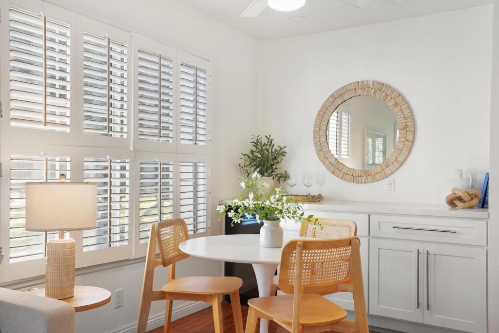 Dining area with a round white table, woven chairs, built-in cabinetry, and tall plantation-shuttered windows.
