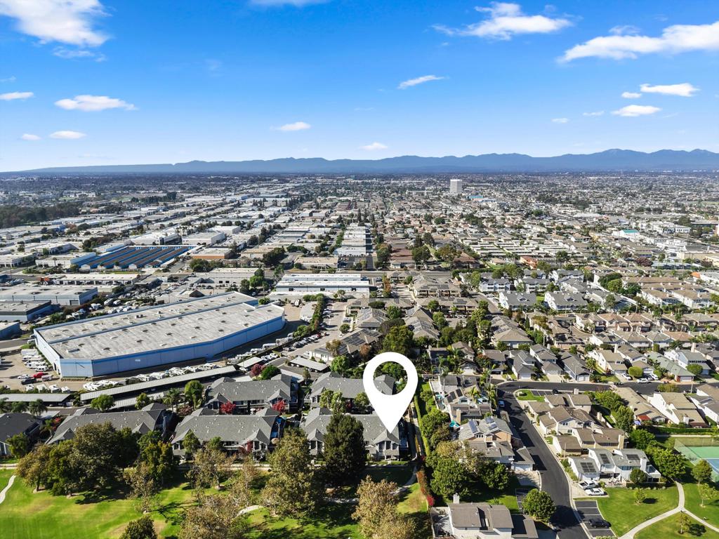 Aerial view of homes with a location marker, green park, industrial buildings, and distant mountains.