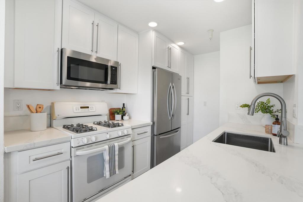 Bright kitchen with white cabinets, stainless steel appliances, and a broad counter with an undermount sink.