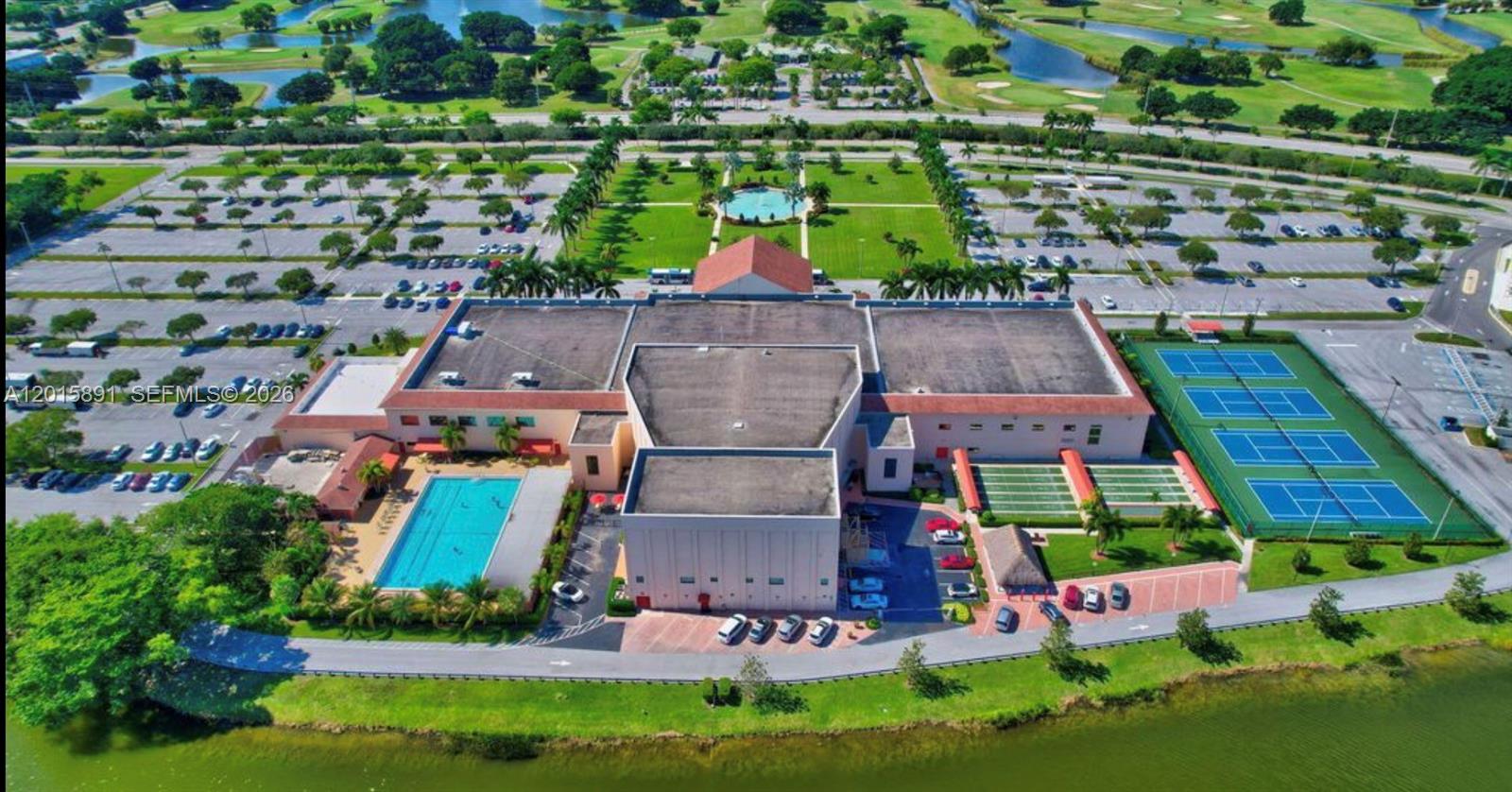 Aerial view of a recreation clubhouse with a swimming pool, tennis courts, and golf course waterways.