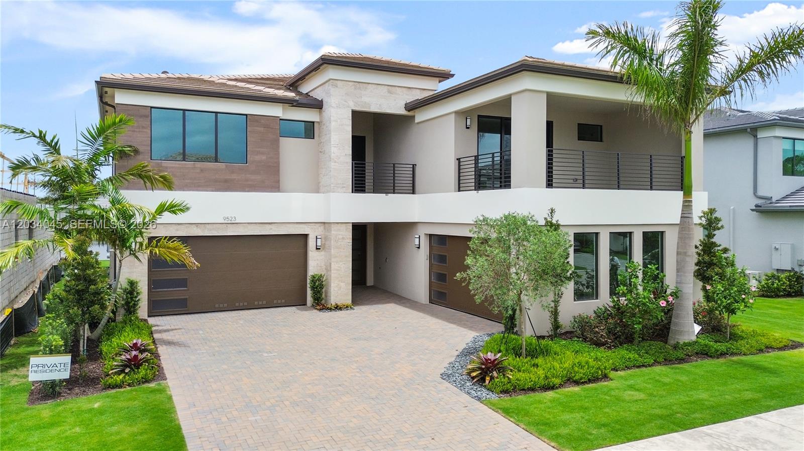 Modern two-story home with a wide paved driveway, balcony, and palm trees.