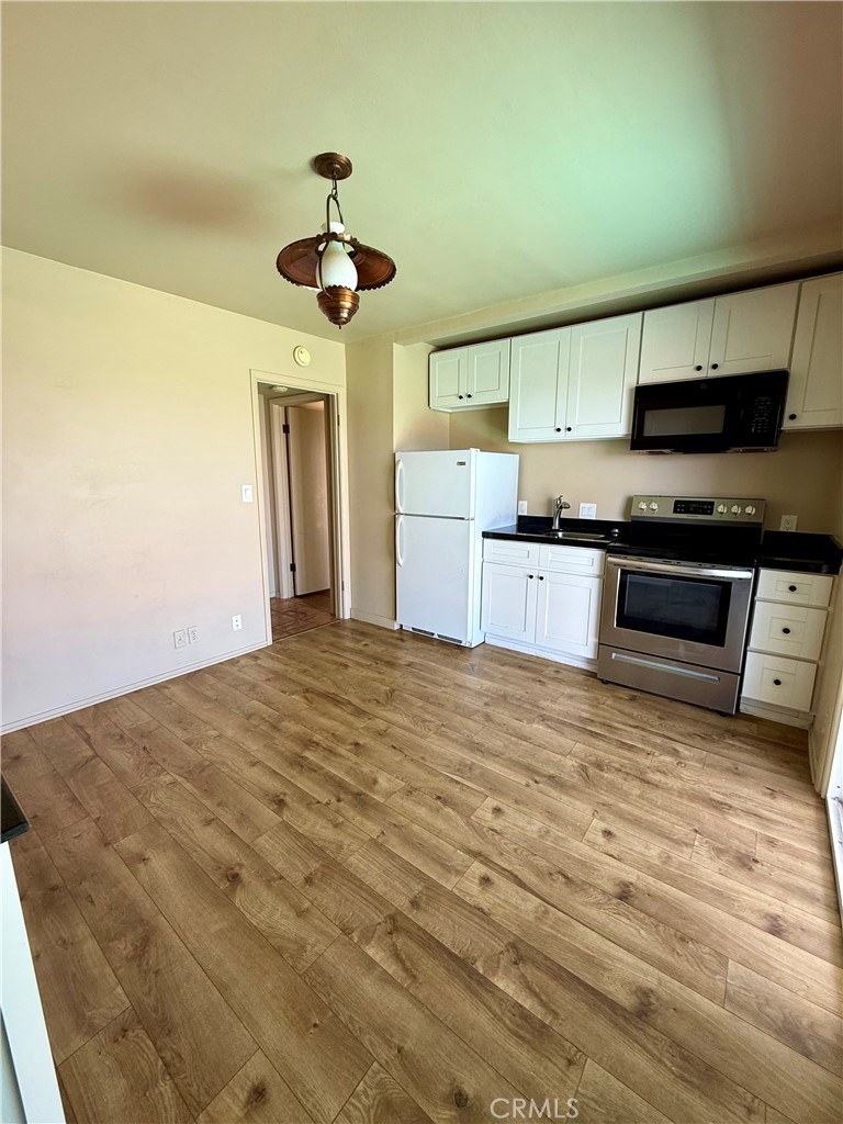 Empty kitchen with white cabinets, a stainless-steel range and microwave, and wood-look plank flooring.