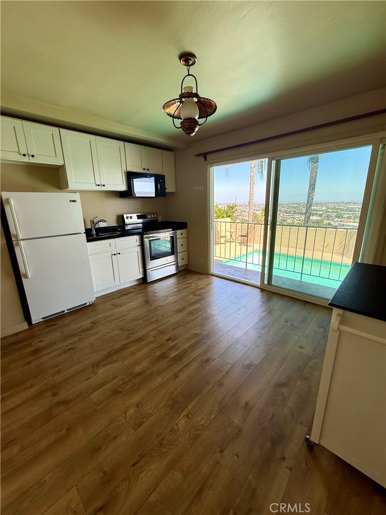 Vacant kitchen with white cabinetry and wood-look floors, opening to a pool and distant city view.
