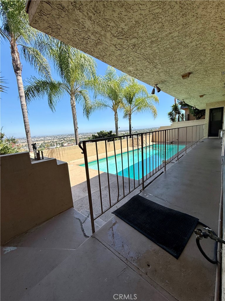 Covered patio overlooks a swimming pool, palm trees, and a distant city view.