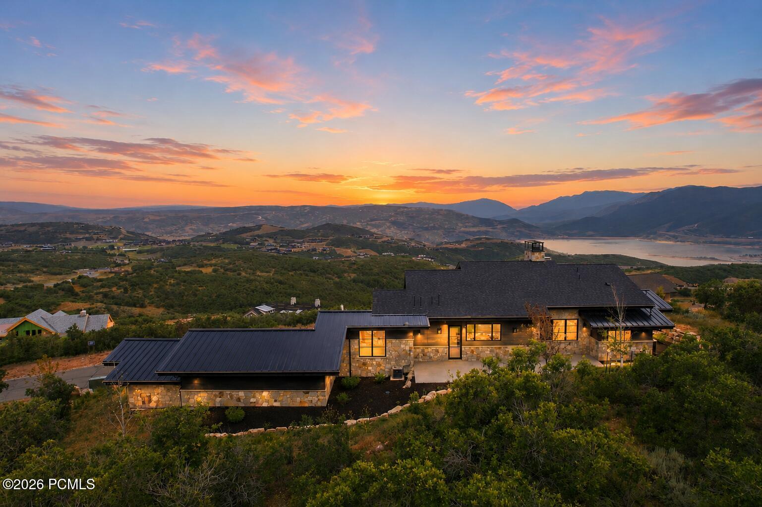 Stone hillside home overlooking a lake and mountains beneath a colorful sunset.