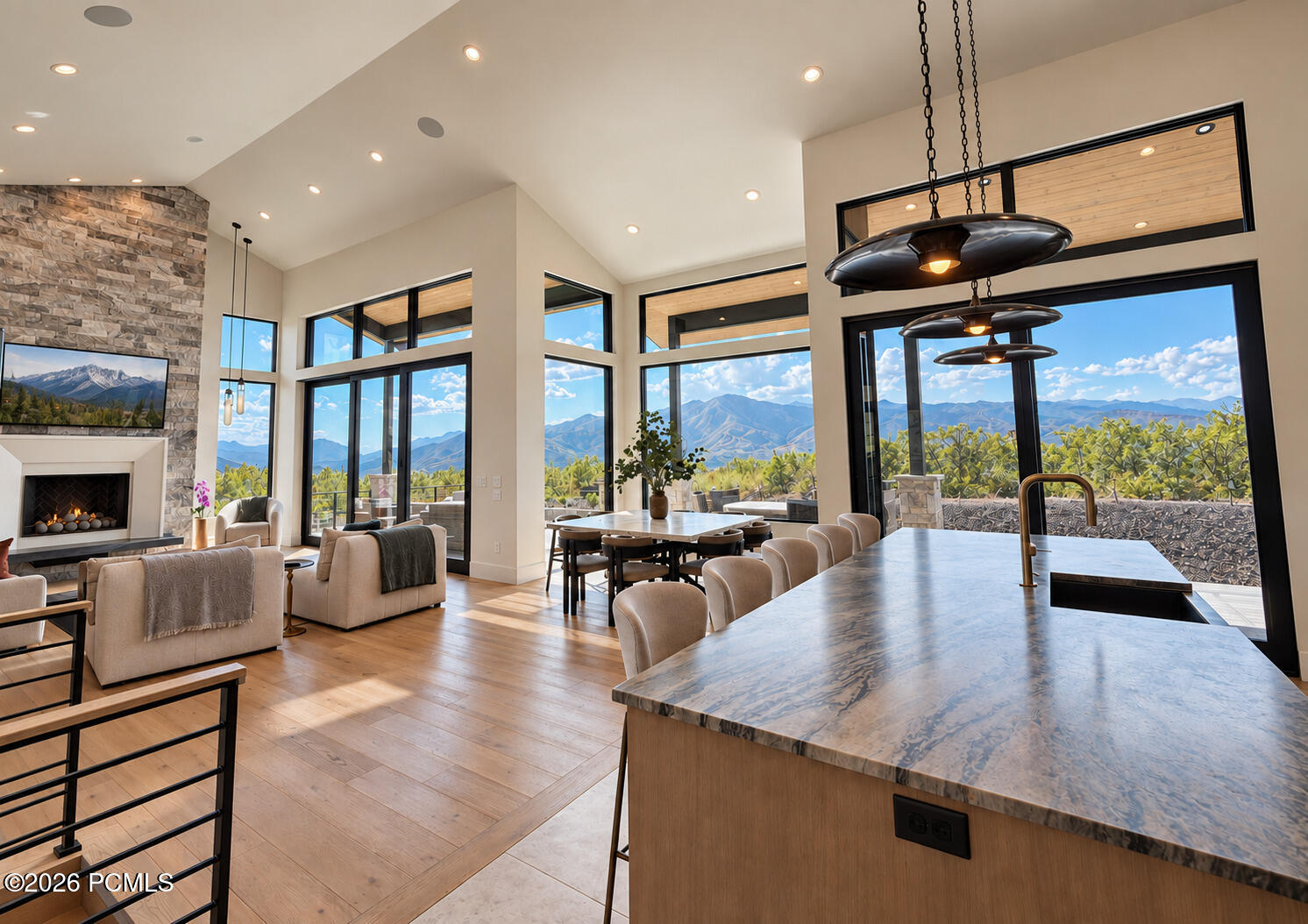 Open-plan living room and kitchen with a stone fireplace, marble island, and mountain views through tall windows.