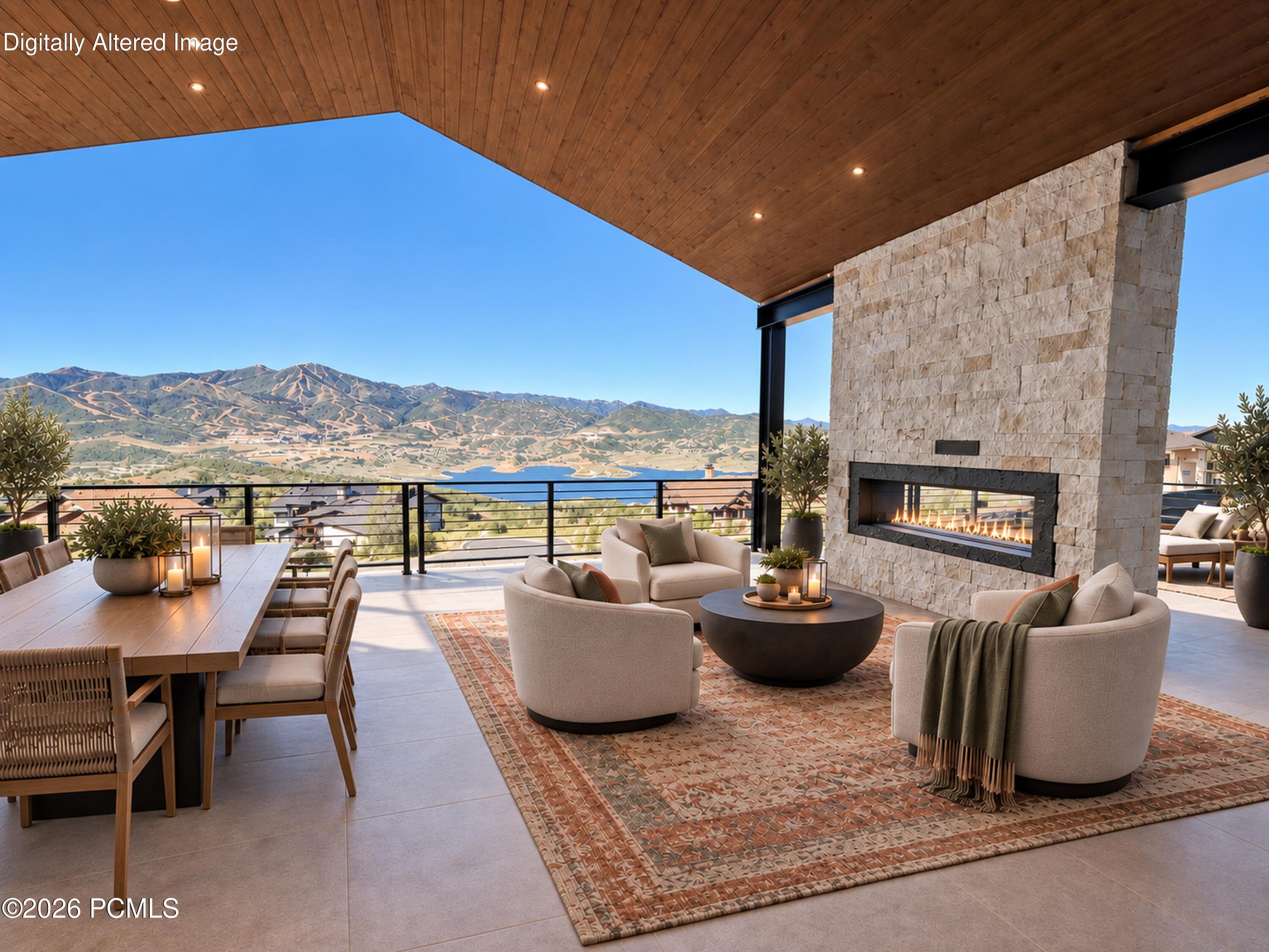 Covered terrace with a stone fireplace and lounge seating overlooking a lake and mountains.