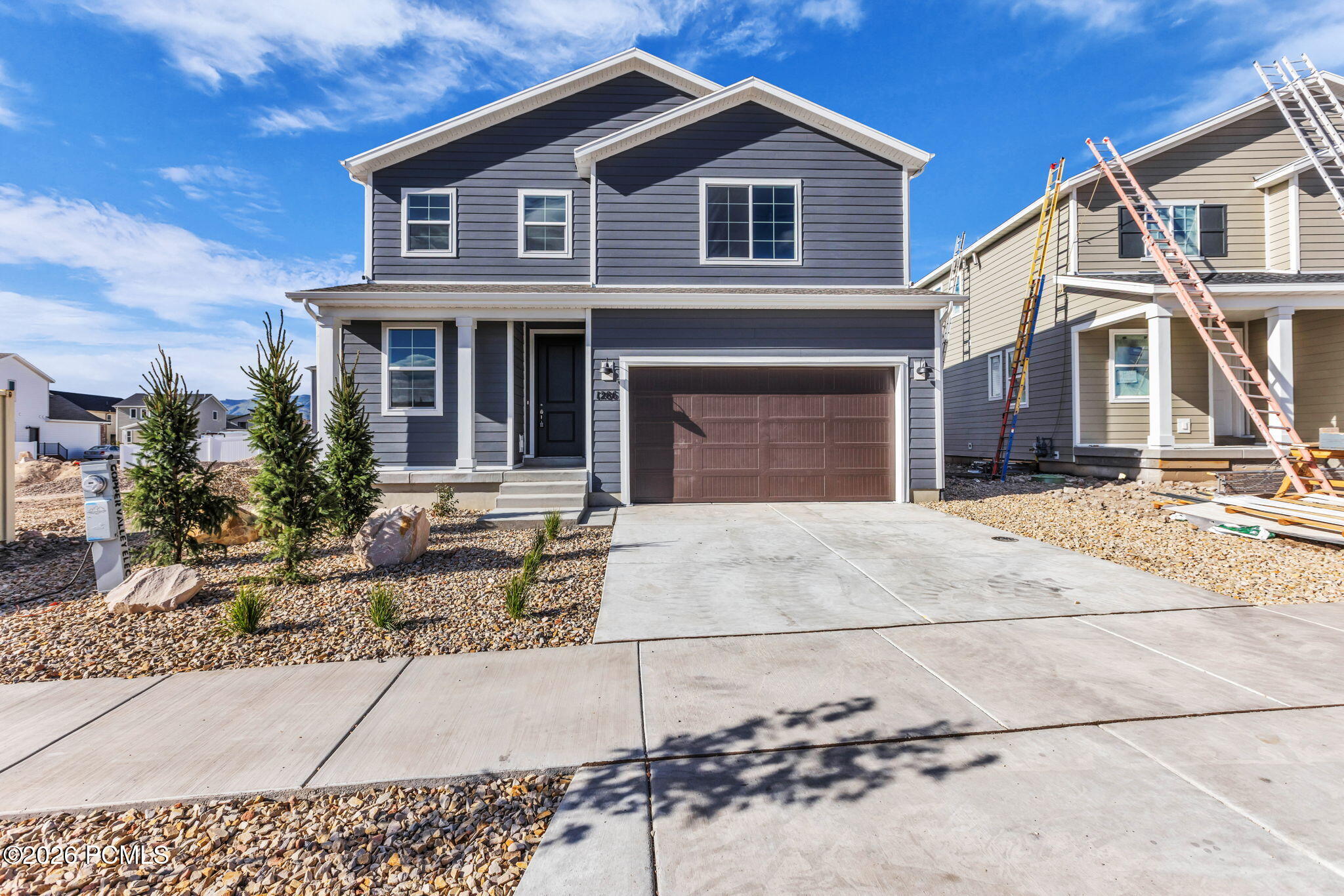 Two-story gray house with a double garage, concrete driveway, and rock landscaping.