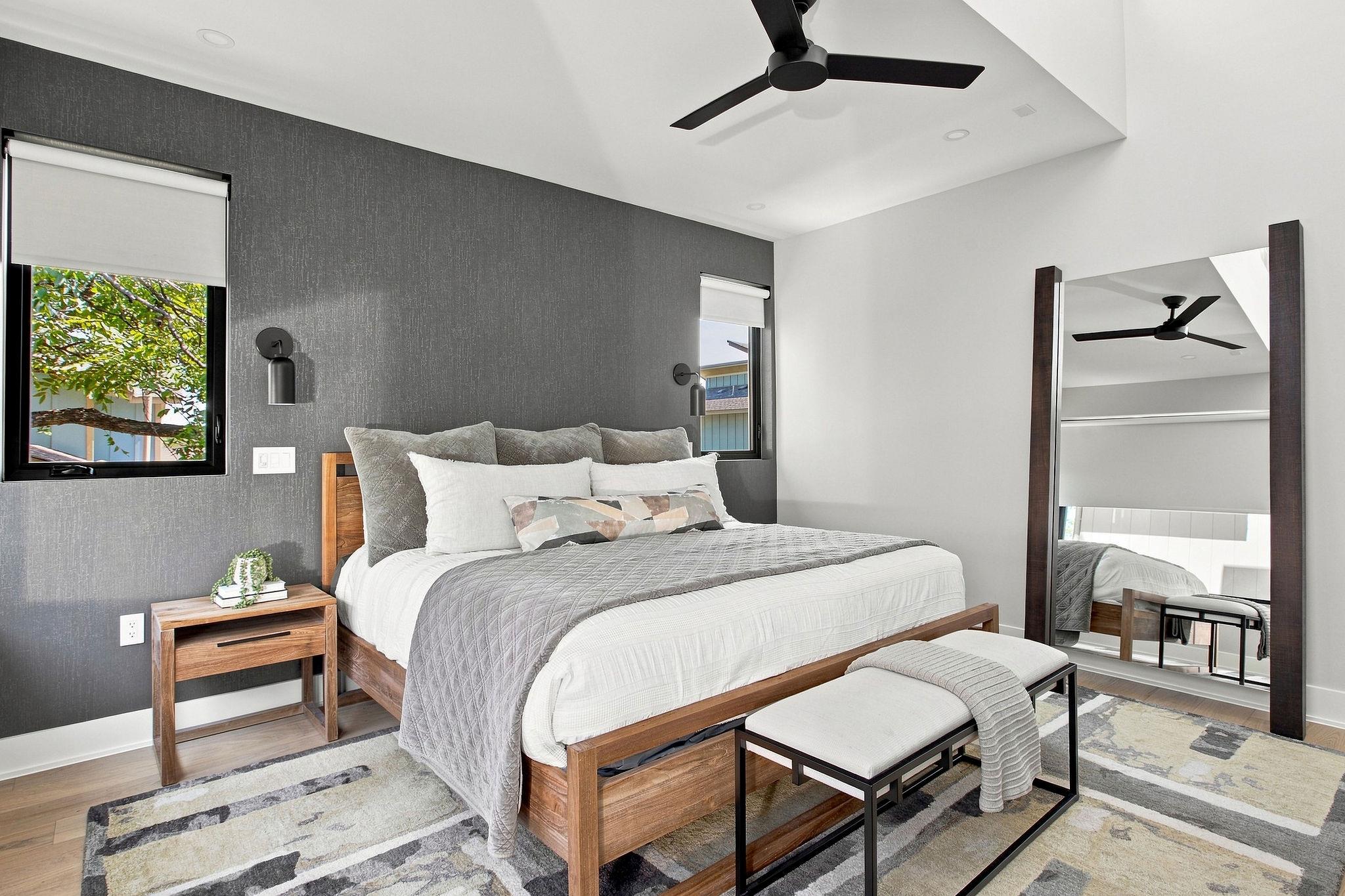 Modern bedroom with a wood platform bed, charcoal accent wall, and full-length mirror.