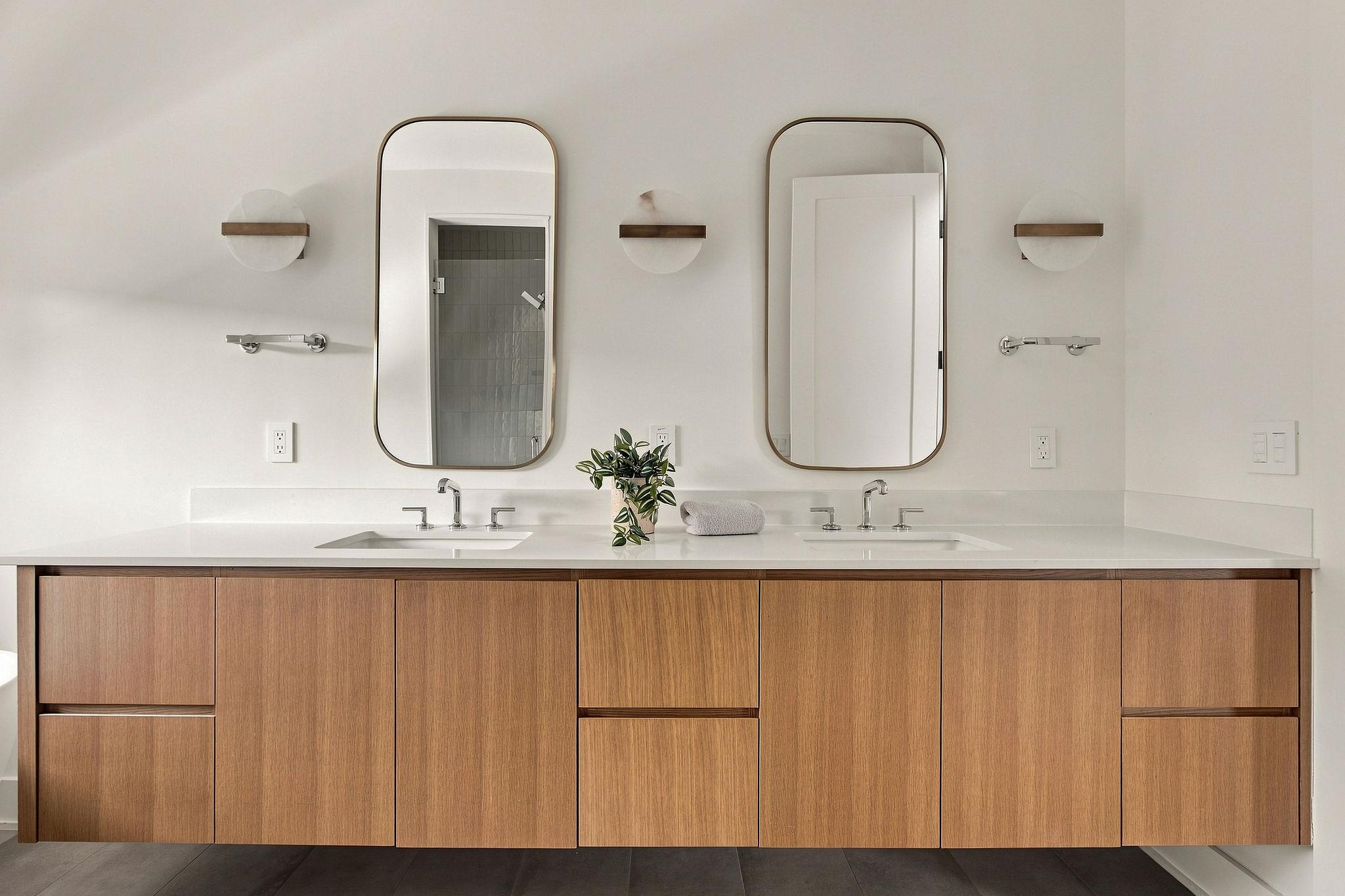 Modern double-sink bathroom vanity with rounded mirrors and warm wood cabinetry.