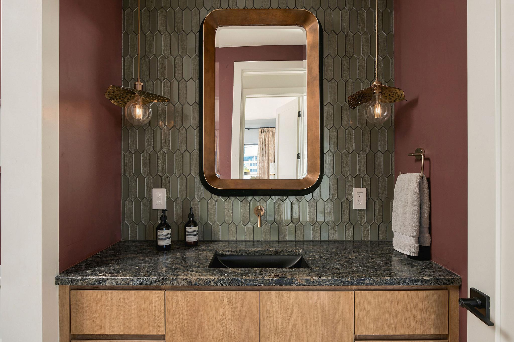 Bathroom vanity with green geometric tile, a bronze-framed mirror, and a dark stone countertop.