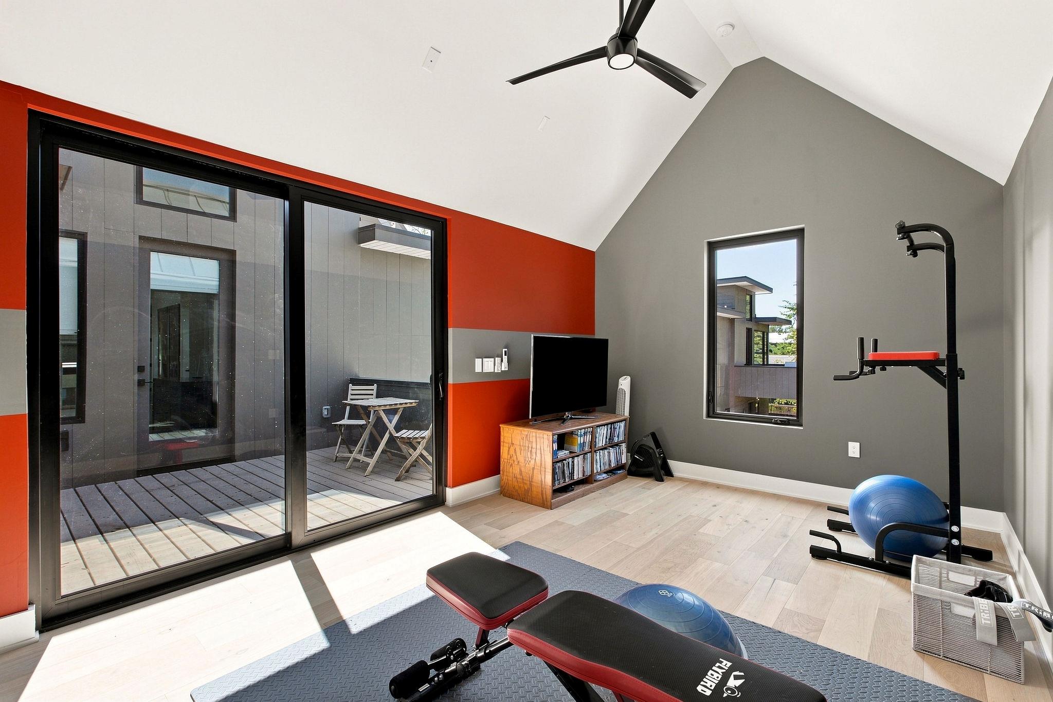 Home gym with a weight bench and exercise equipment beside sliding glass doors to a deck.