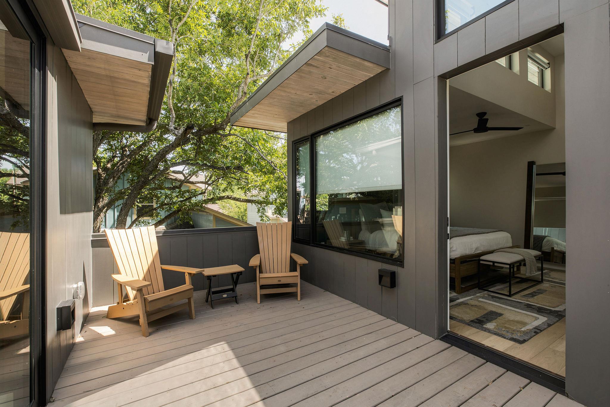Raised wood deck with Adirondack chairs beside an open doorway to a bedroom.