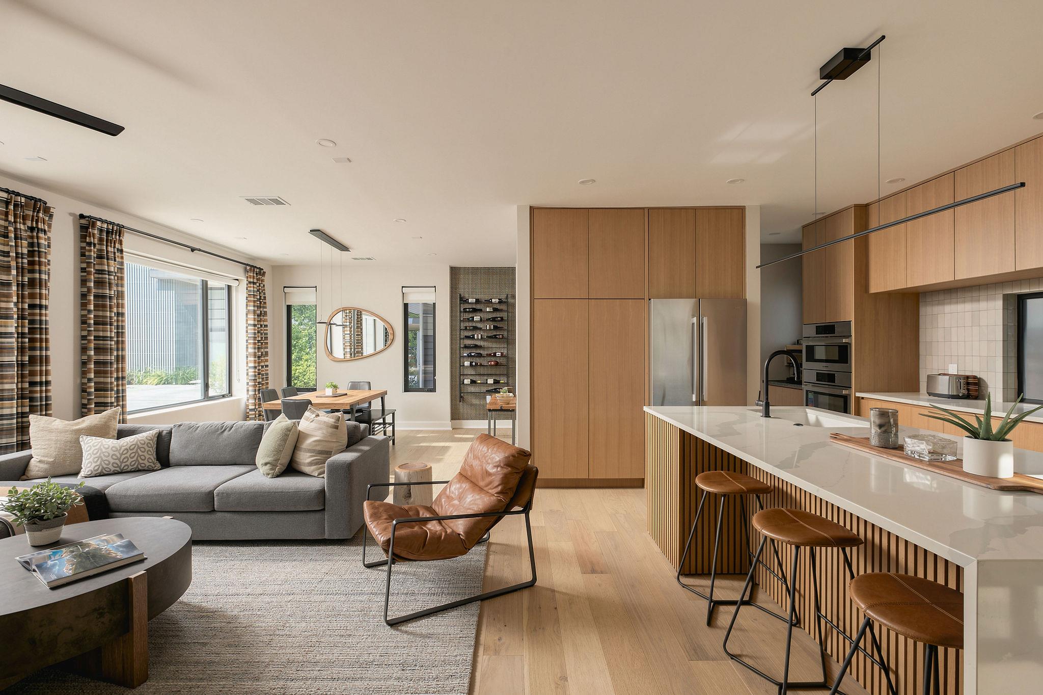 Open-plan living room and kitchen with wood cabinetry, a large island, and windows beside a gray sectional.
