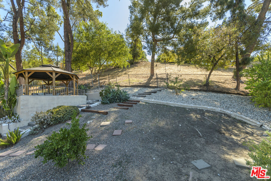 Backyard with a covered wooden gazebo, gravel landscaping, and mature trees.