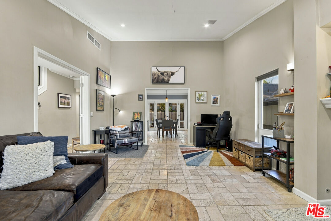 Living room with tiled floors, leather sofa, desk, and adjoining dining area.