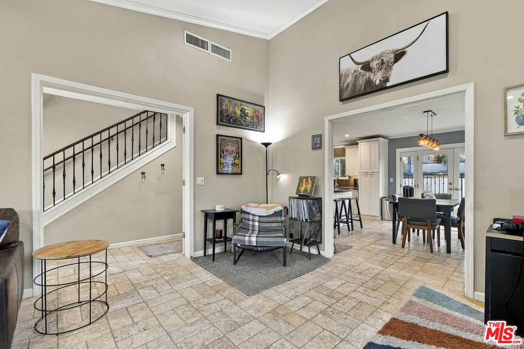 Living room with tiled floors, an iron-railed staircase, and dining area beyond.