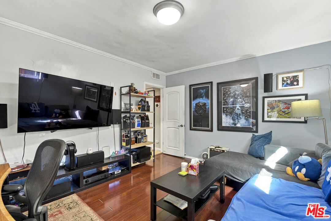 Living room with a wall-mounted TV, framed artwork, hardwood floors, and a gray sectional sofa.