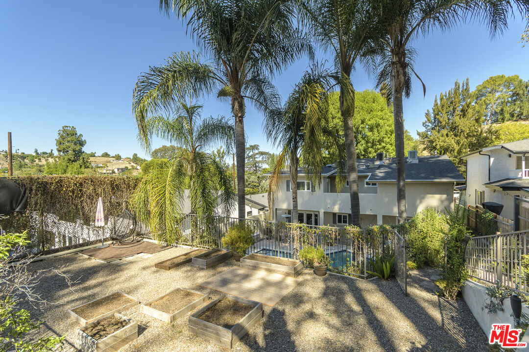 Backyard with a fenced pool, gravel patio, raised garden beds, and tall palm trees.