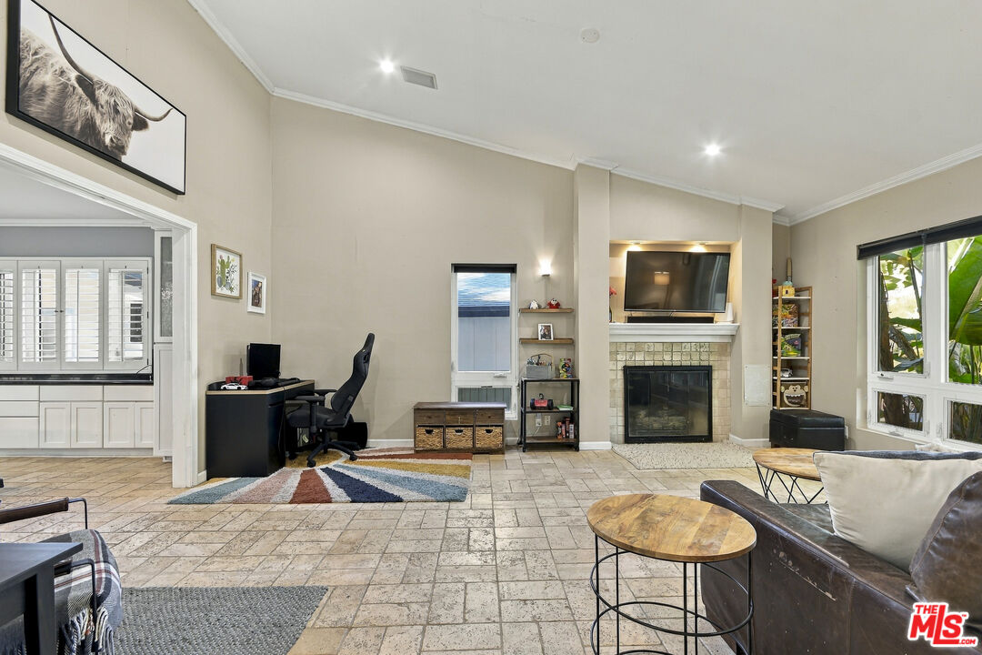 Living room with a tiled floor, fireplace, television, and large windows.