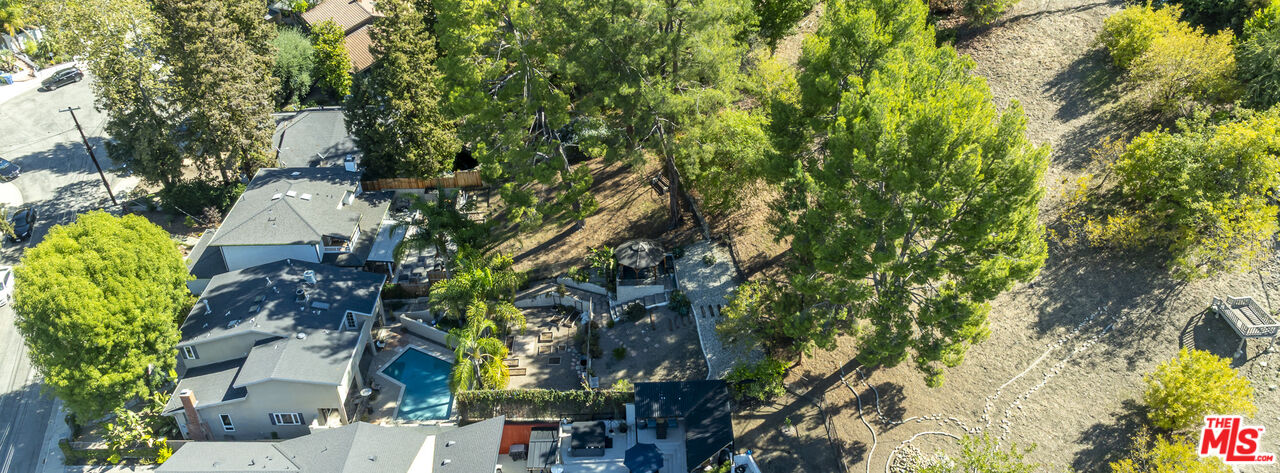 Aerial view of a home with a backyard pool beside a tree-covered hillside.