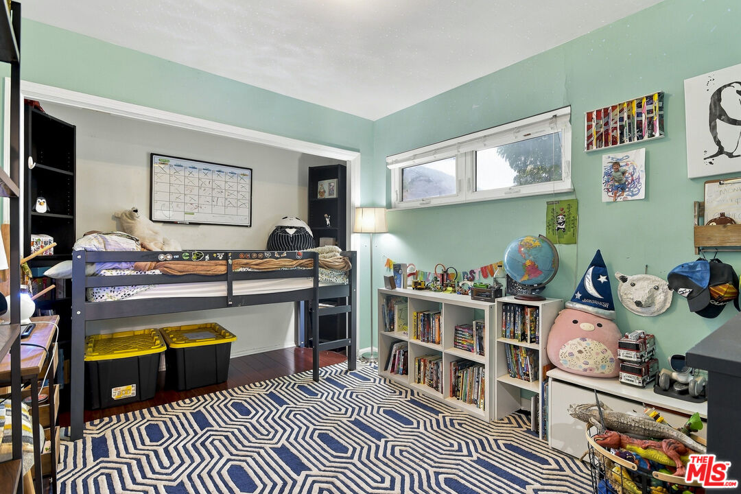 Bedroom with a black bunk bed, mint-green walls, bookcases, and a blue-and-white geometric rug.