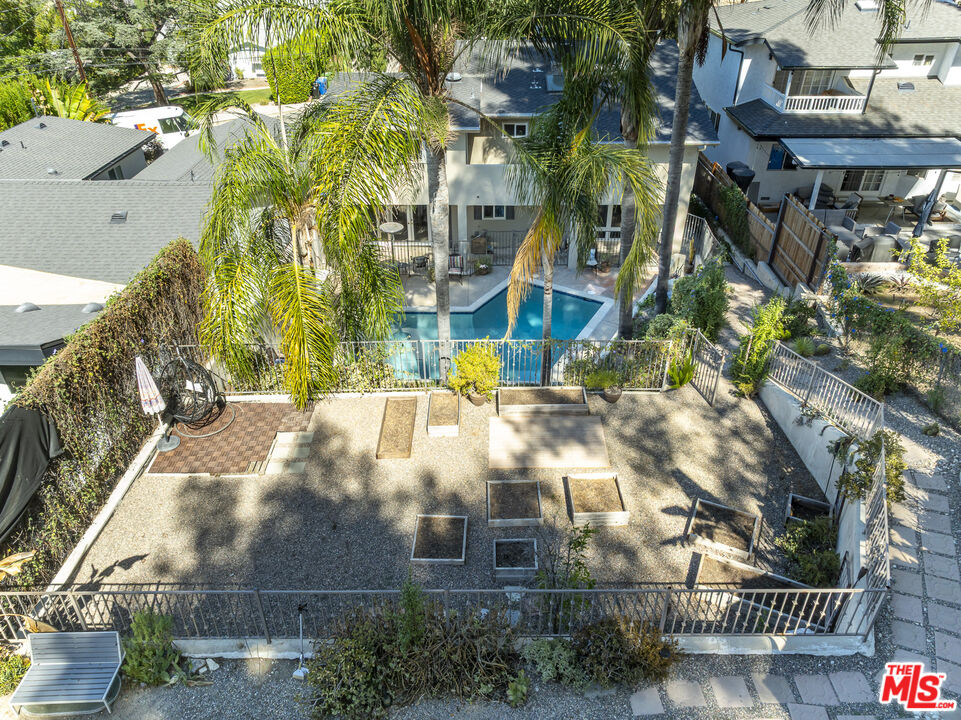 Aerial view of a backyard with a swimming pool, tall palms, and raised garden beds.