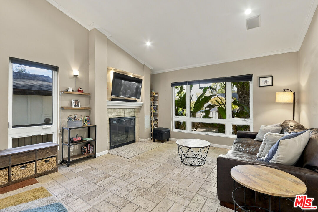 Living room with vaulted ceiling, tiled floor, fireplace, large windows, and dark leather sectional.