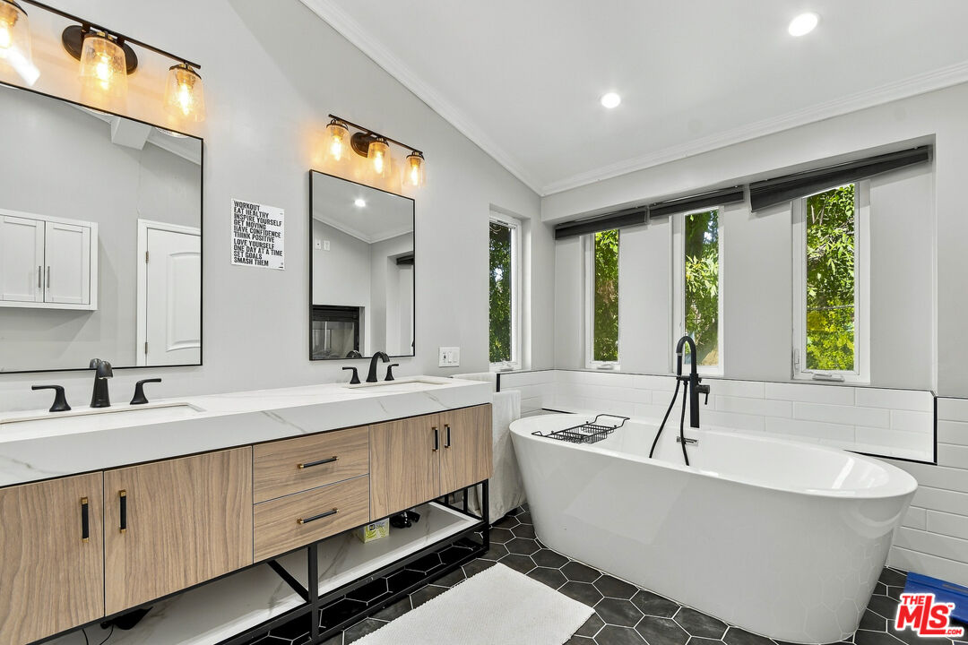 Modern bathroom with a freestanding tub, double vanity, and tall windows overlooking greenery.