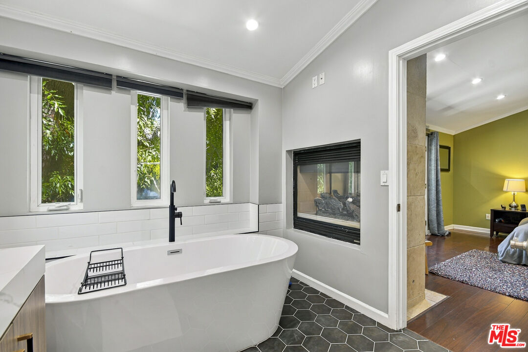 Bathroom with a freestanding soaking tub, narrow windows, wall-mounted fireplace, and dark hexagonal tile floor.