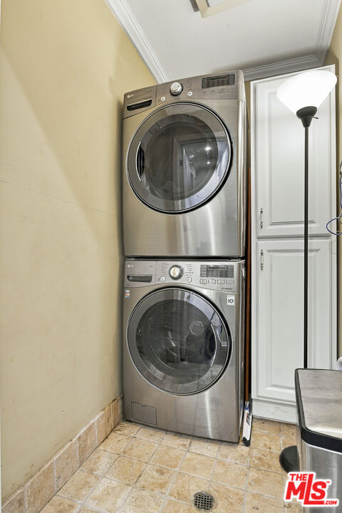 Stacked stainless steel washer and dryer beside a white cabinet in a tiled laundry area.