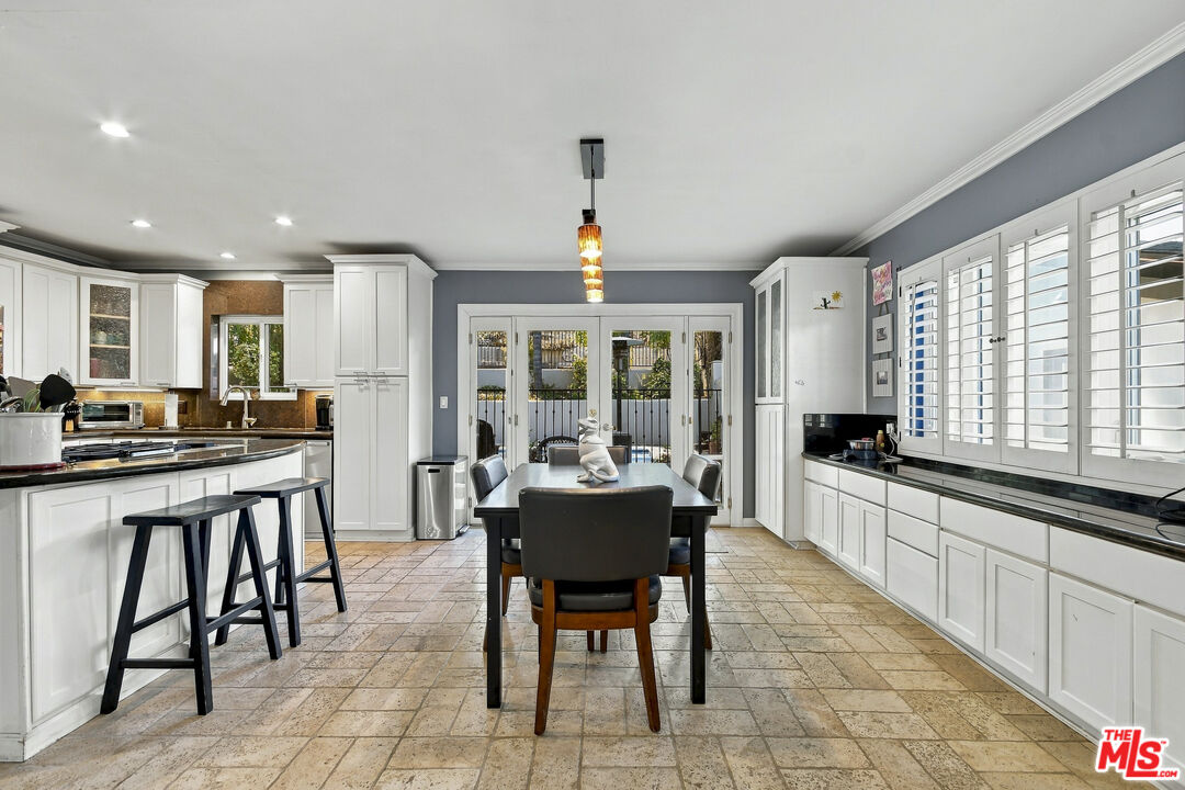 Kitchen and dining area with white cabinets, a breakfast bar, shuttered windows, and glass doors to the pool.
