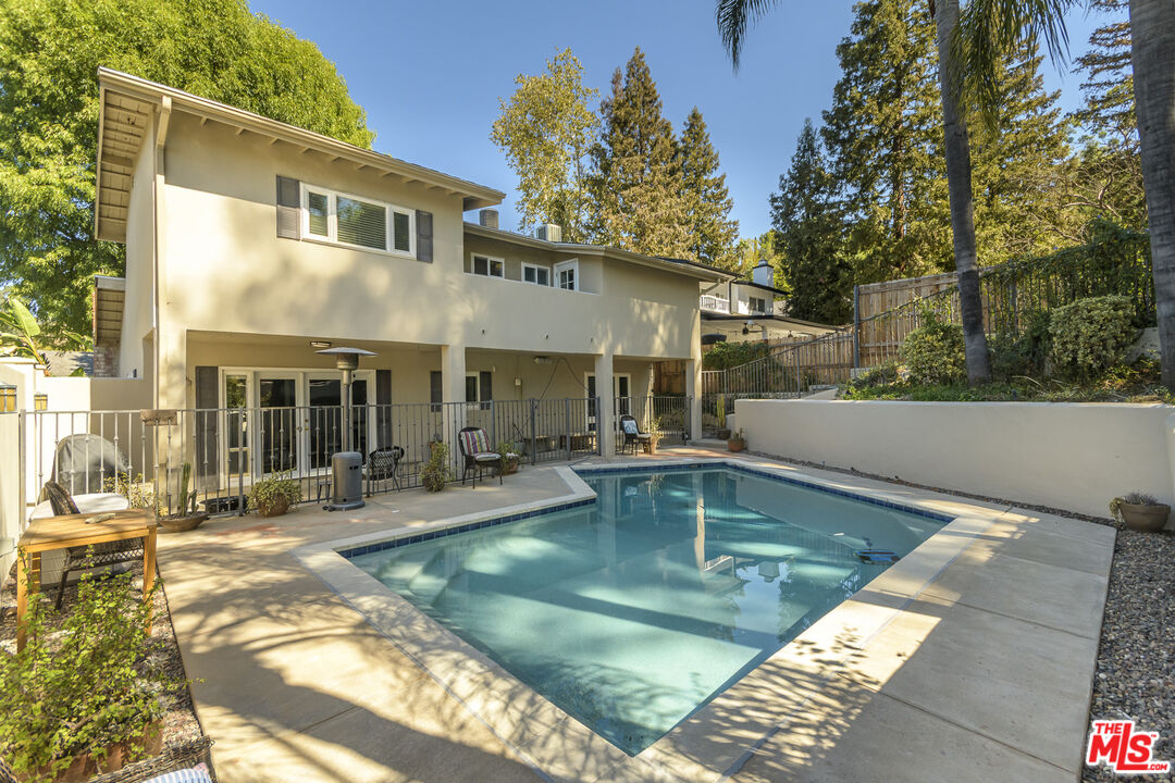 Back of a two-story home with a rectangular swimming pool, patio seating, and mature trees.