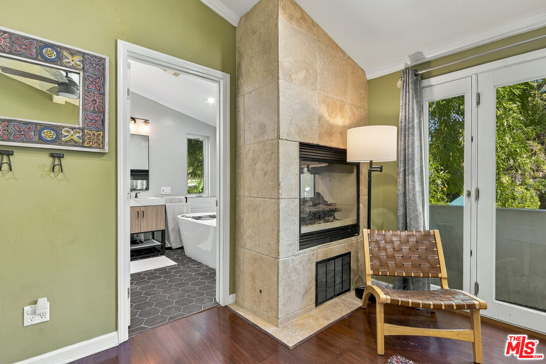Furnished sitting area with a tall stone fireplace, woven chair, and glass doors beside a bathroom doorway.