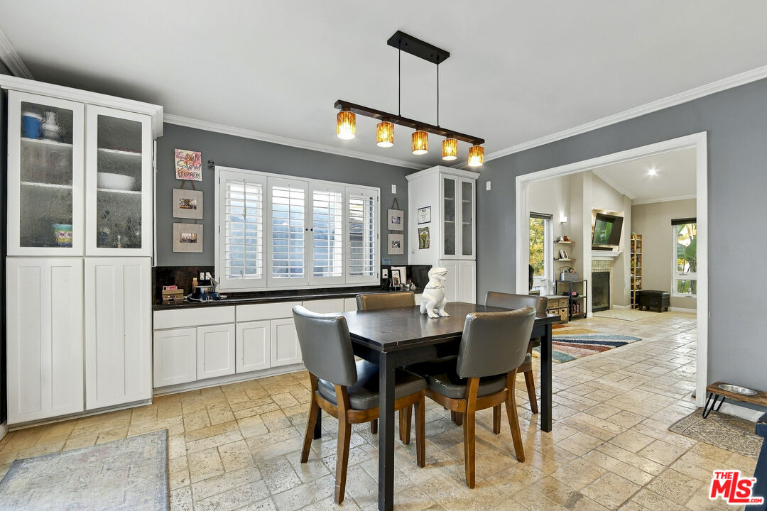 Dining room with white built-ins, shuttered windows, a dark table, and tan tile flooring.
