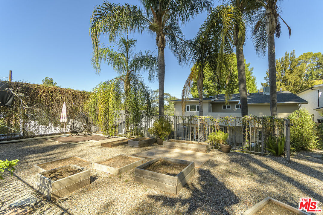 Backyard with raised garden beds, gravel landscaping, tall palms, and a fenced patio.