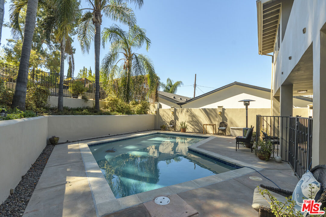 Backyard swimming pool with a paved patio, lounge chairs, and tall palm trees.