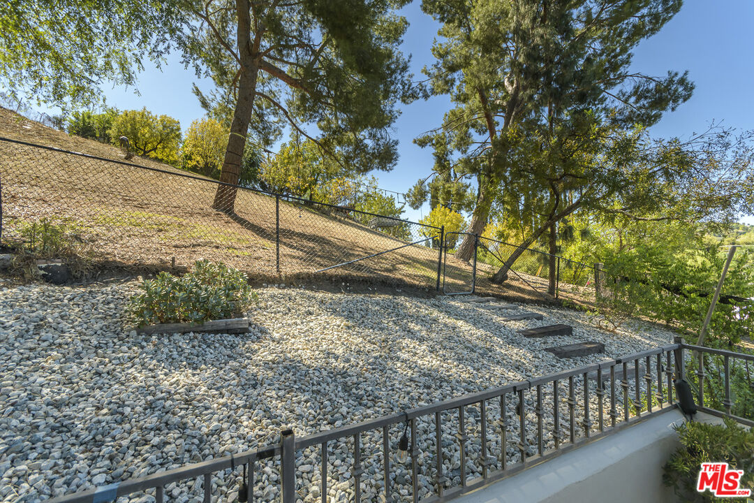 Rock-covered sloping backyard with a chain-link fence and mature trees.