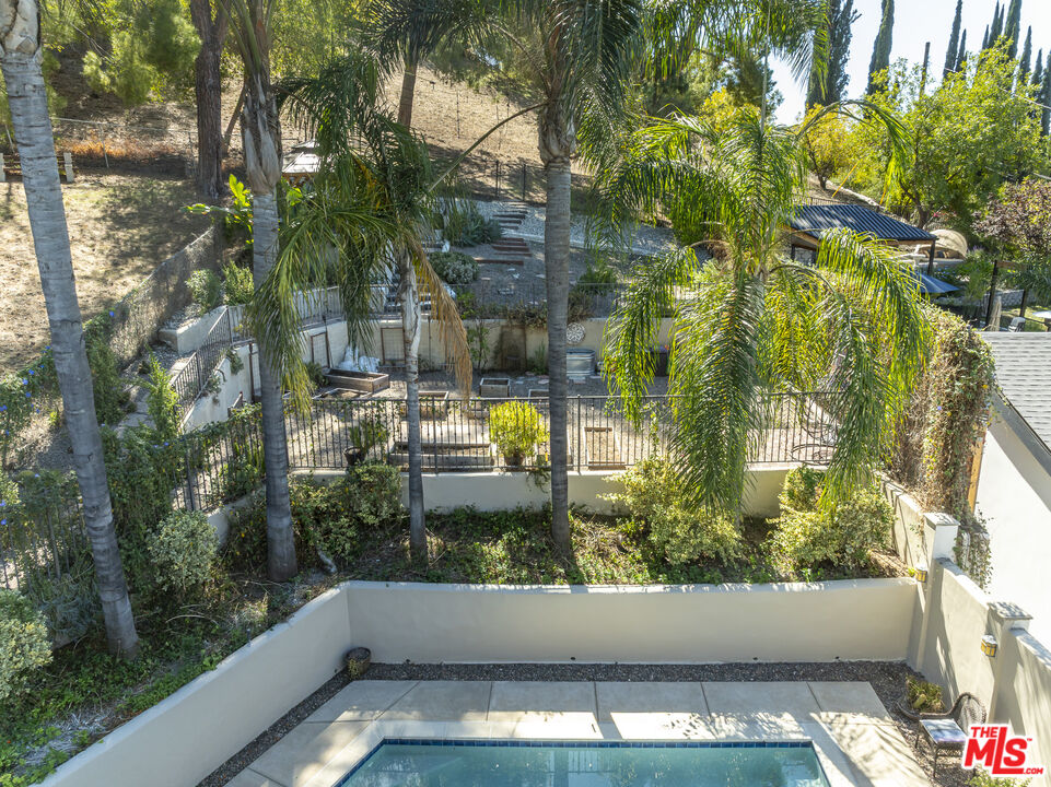 Backyard pool and patio bordered by tall palms, a fenced garden, and a hillside.