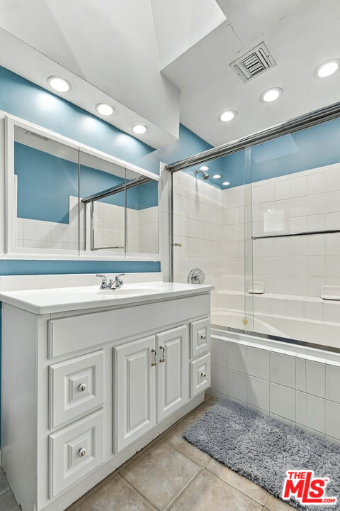 Bathroom with a white paneled vanity, blue accent walls, and a glass-enclosed tiled tub and shower.